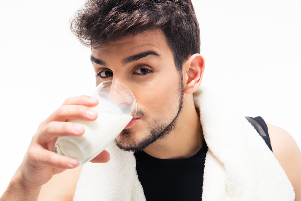 Sports man with towel drinking milk isolated on a white background. Looking at camera